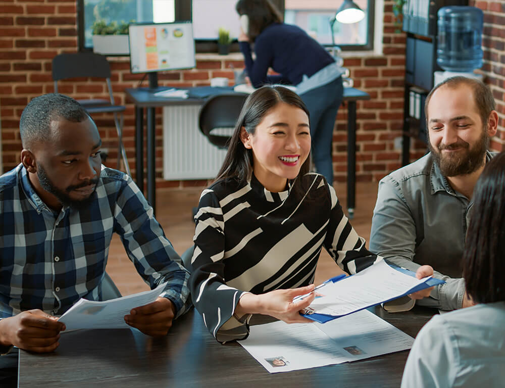 A group of young professionals sitting at a table having a team meeting with papers on the table