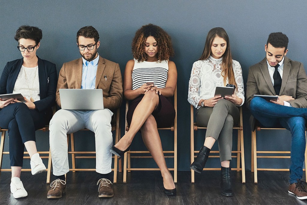 Five young professional people sitting in chairs in a straight line against a blue wall