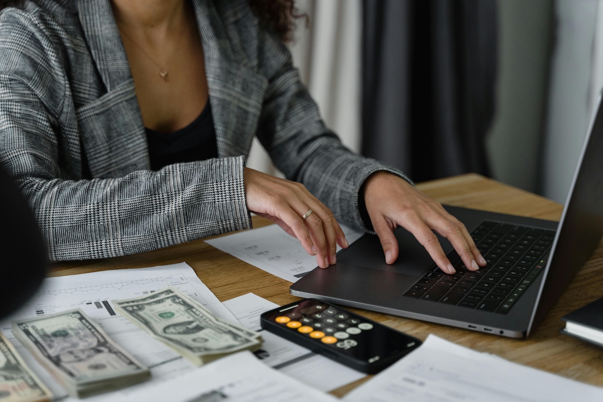 payroll Close up of woman's hands on laptop keyboard with money, paperwork, and calculator next to her