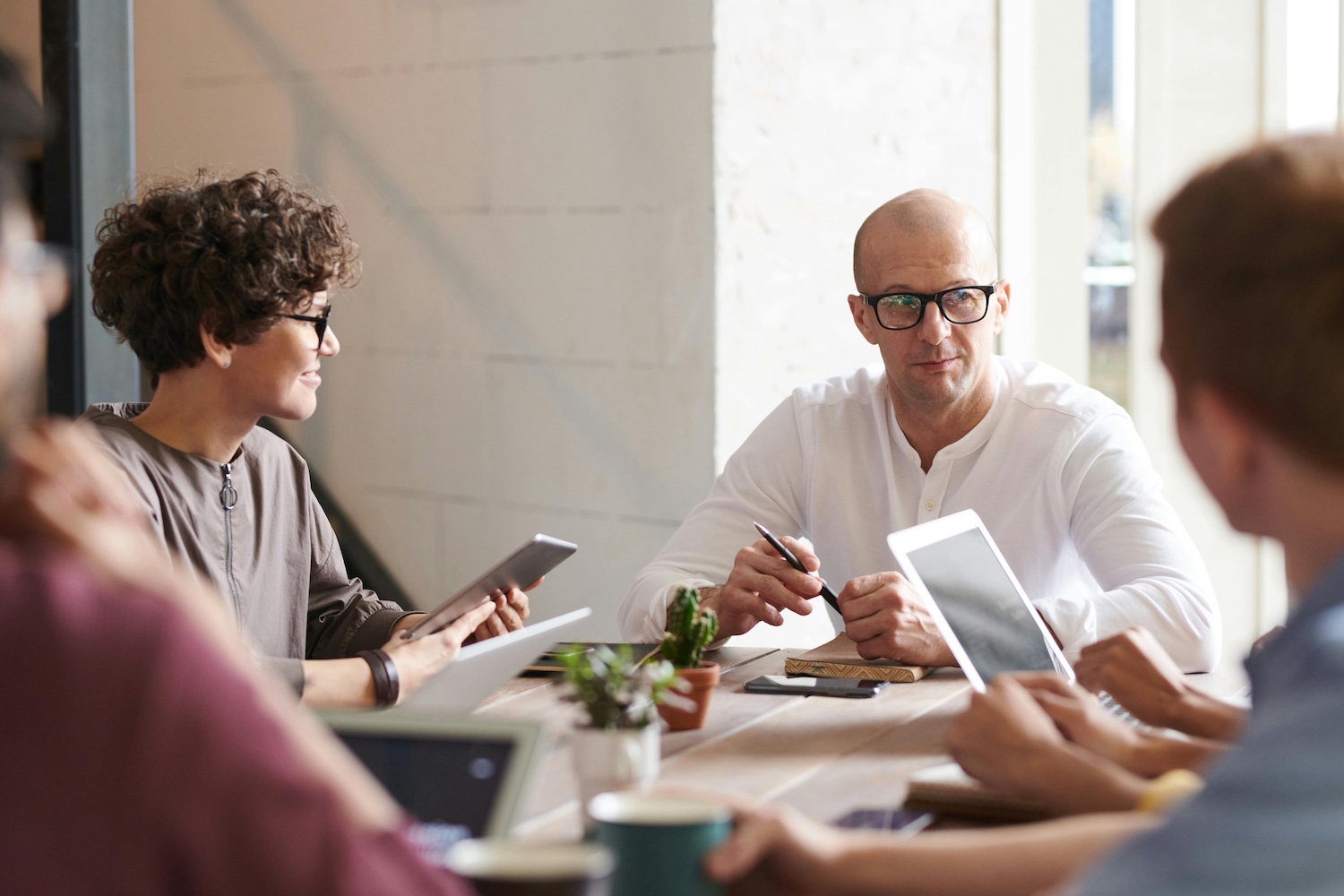 A group of professionals sitting at a table having a team meeting with tablets and laptops