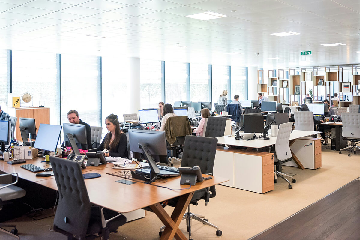 A Large, Open Floor Plan Office Space with Ceiling to Floor Windows, People Sitting at Their Communal Desks